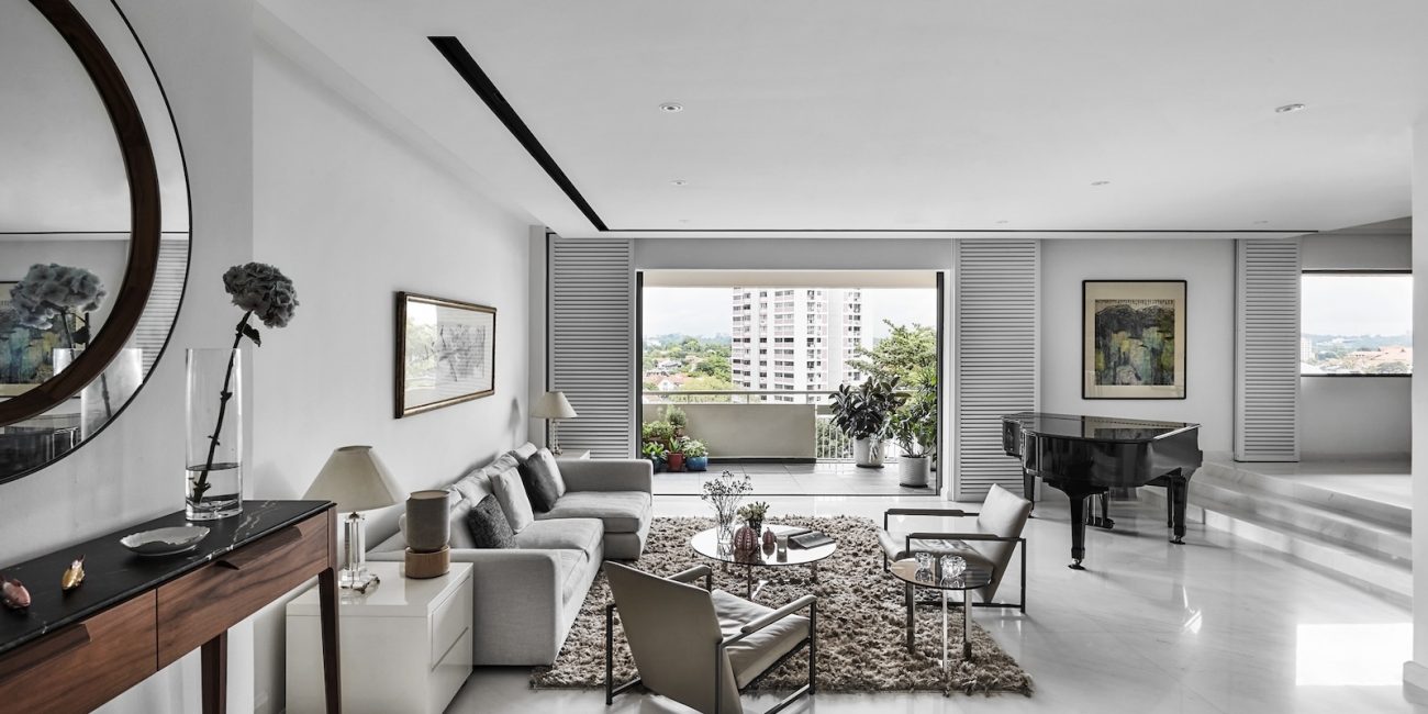 A modern living room with a sofa, armchairs, a coffee table, a console table with a round mirror, art on the walls, a piano, and large windows offering a city view.